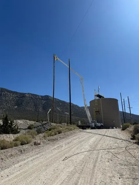 Utility poles and field vehicles beside a hillside