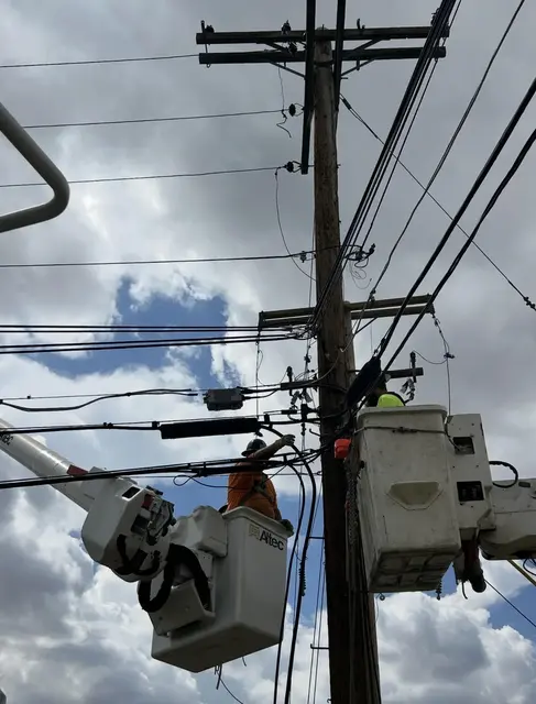 Line workers in buckets beside overhead conductors