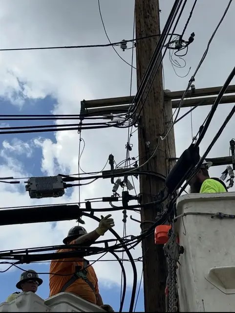 Bucket trucks and workers beside a utility pole